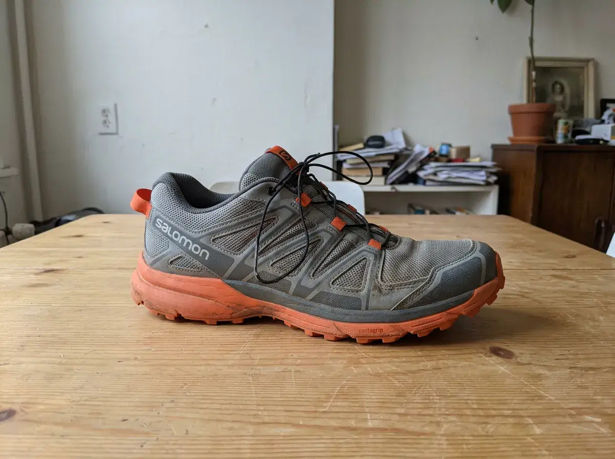 A plain phone photo of a grey and orange trail running shoe on a wooden table